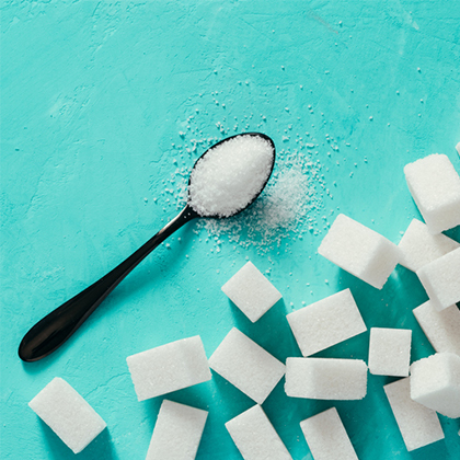 White sugar in a spoon next to numerous sugar cubes